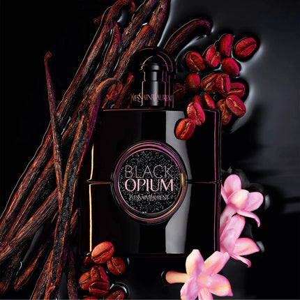 A black perfume bottle labeled 'Black Opium' by Yves Saint Laurent, styled with vanilla beans, coffee beans, and pink orchids on a glossy black background.